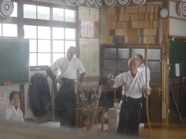 Japanese archer in martial arts clothes, holding bow and reaching
for arrow.
2 Japanese men standing,
one lady sitting, all in white cloths 